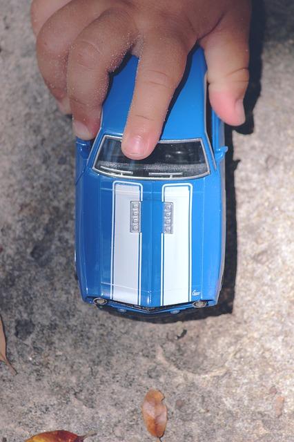 Childs hand on blue toy car with two white stripes