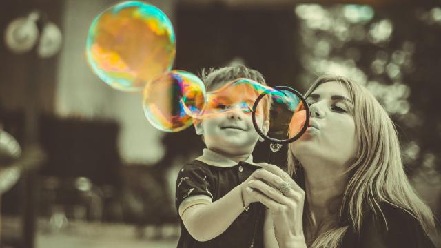 Lady blowing bubbles for young boy, image in sepia with colour effect on bubbles
