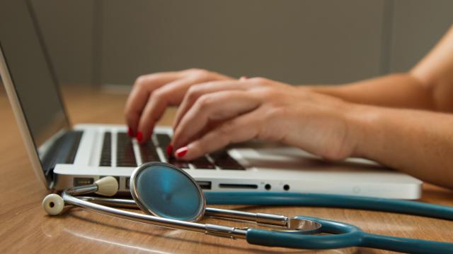 Photo of hands typing on laptop next to stethoscope 