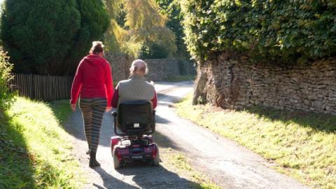 Lady walking with gentleman in mobility scooter