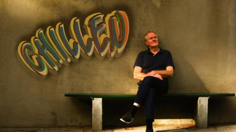 Man sat on a bench with graffiti on wall saying 'chilled'