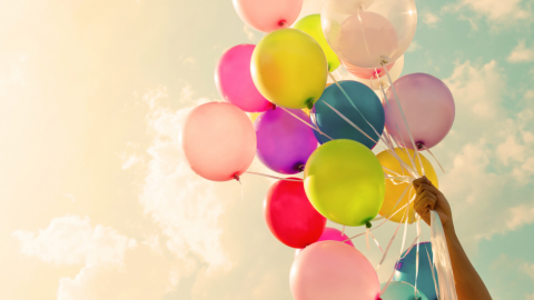 Colourful balloons help up in the air with a pink toned clouded background
