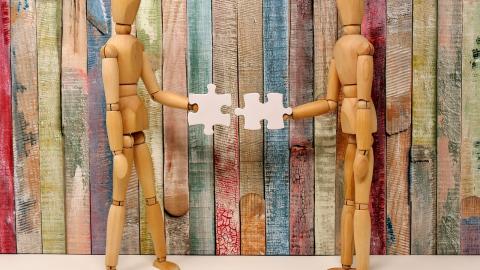 Two wooden mannequins connecting jigsaw pieces