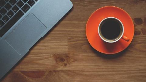 Laptop and black coffee in orange cup and saucer