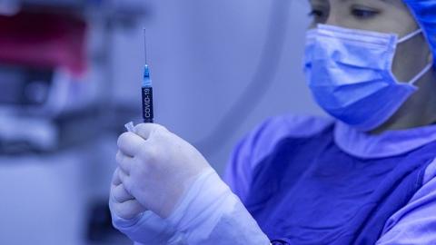 Nurse in full scrubs and mask holding needle with Covid vaccine