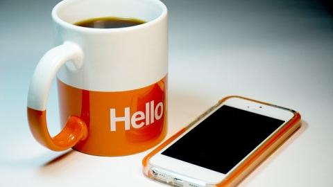 Mug of coffee with orange band around bottom with words 'hello' printed in white next to mobile phone in orange case