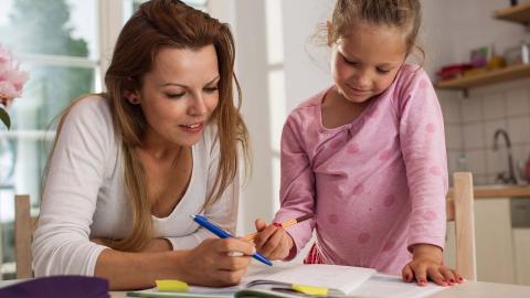 Lady looking at notebook holding a blue pen with child in pink top