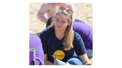 Charlotte Lawson on beach in Kinship logo t-shirt with sunglasses on top of head