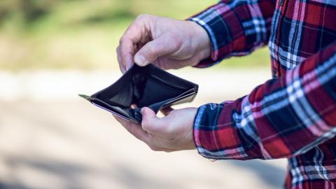 Person in checked shirt stood at right of photograph (upper and lower body off camera) holding empty wallet open.