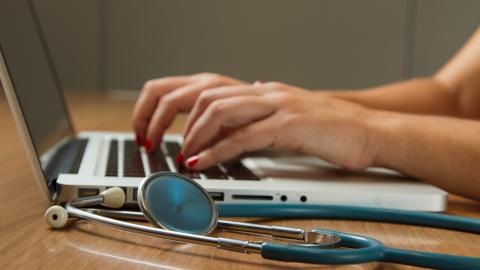 Photo of hands typing on laptop next to stethoscope 
