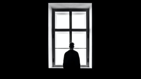 Black and white image of person in front, facing, of large window.