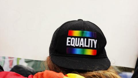 Equality pride cap on backwards and pride flag wrapped around person facing away from camera