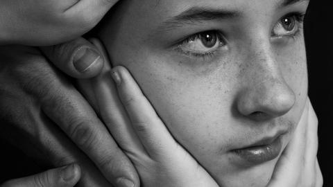 Teen boy with head in hands and various hands on him 